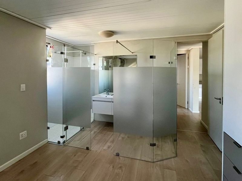 Modern bathroom featuring a glass-enclosed shower, vanity with basin, and frosted glass partitions, finished with light wood-look laminate flooring.