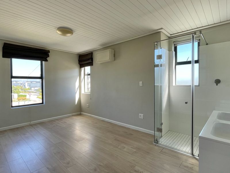 A bright, empty bedroom featuring light laminate flooring, a tongue and groove ceiling, and a modern en-suite shower with a glass enclosure.