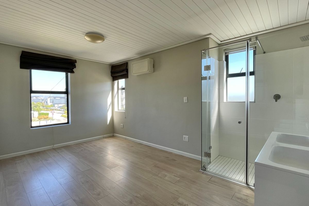 A bright, empty bedroom featuring light laminate flooring, a tongue and groove ceiling, and a modern en-suite shower with a glass enclosure.