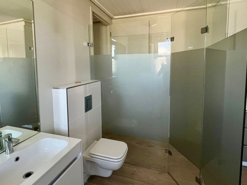 Modern bathroom featuring a wall-hung toilet with concealed cistern, glass shower enclosure, vanity basin with mixer tap, and built-in cabinetry.