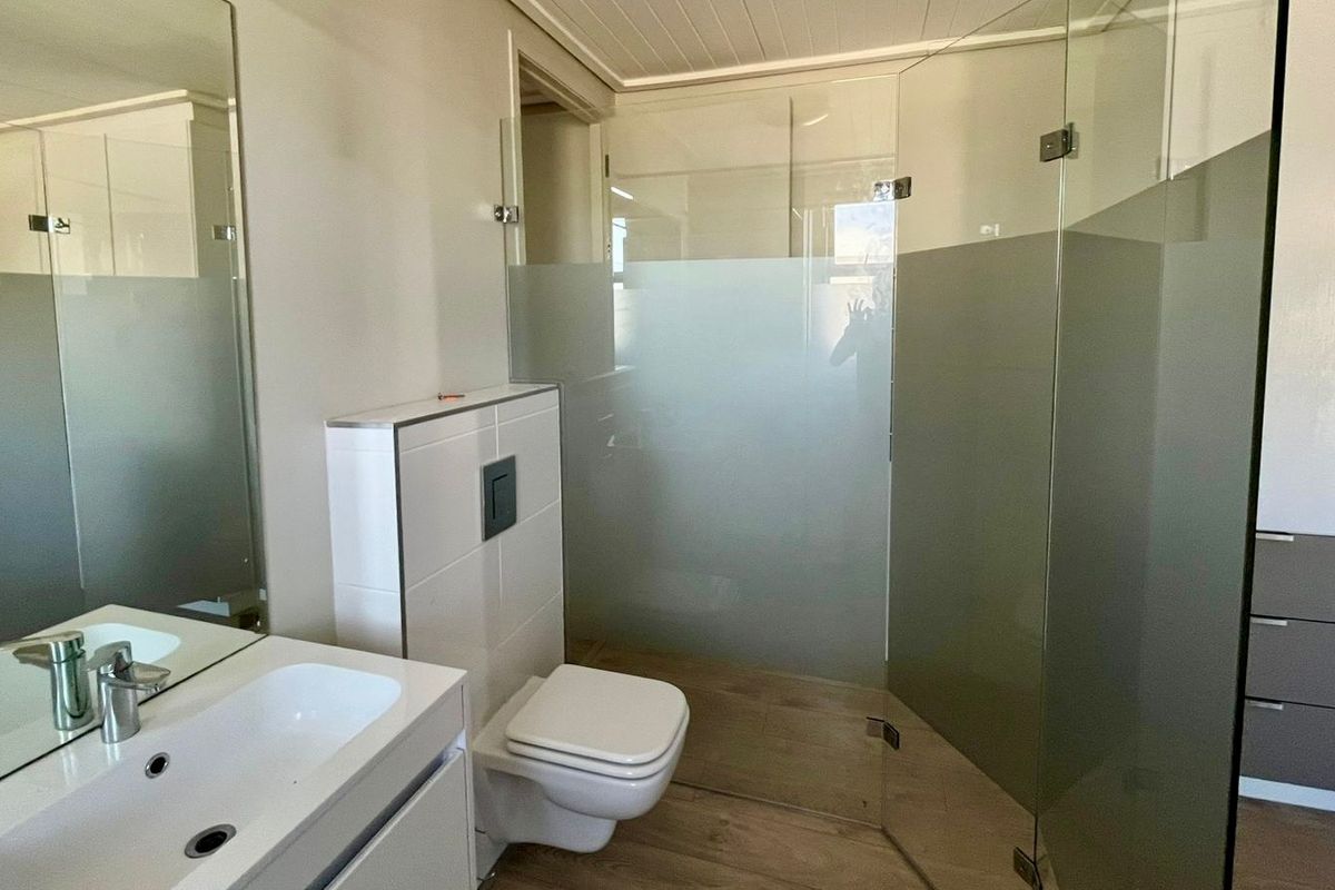 Modern bathroom featuring a wall-hung toilet with concealed cistern, glass shower enclosure, vanity basin with mixer tap, and built-in cabinetry.