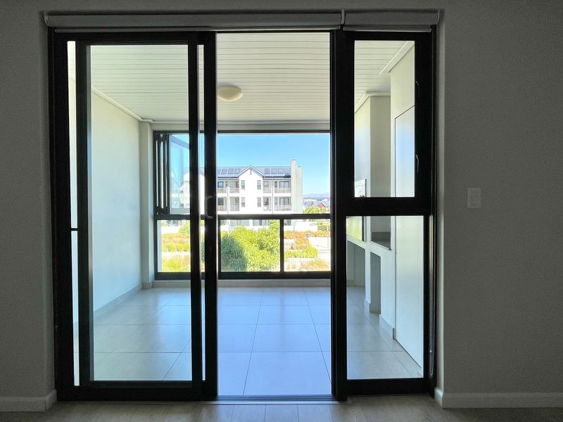 A bright, empty balcony featuring tiled flooring and large sliding glass doors, offering an open-air space accessible from the main living area.