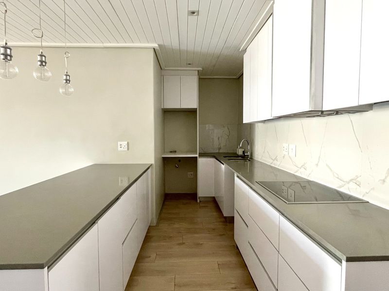 Modern, minimalist kitchen featuring sleek white cabinetry, stone countertops, integrated induction hob, and wood-look tile flooring in a clean, open-plan layout.