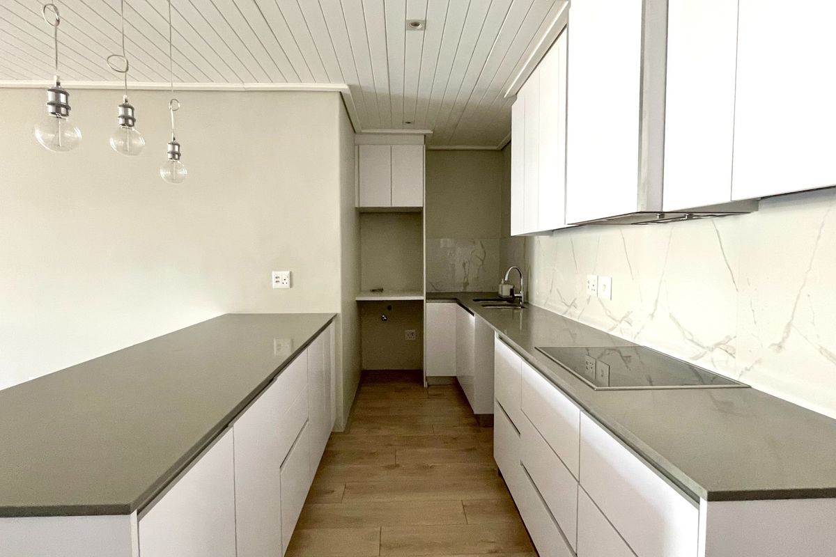 Modern, minimalist kitchen featuring sleek white cabinetry, stone countertops, integrated induction hob, and wood-look tile flooring in a clean, open-plan layout.