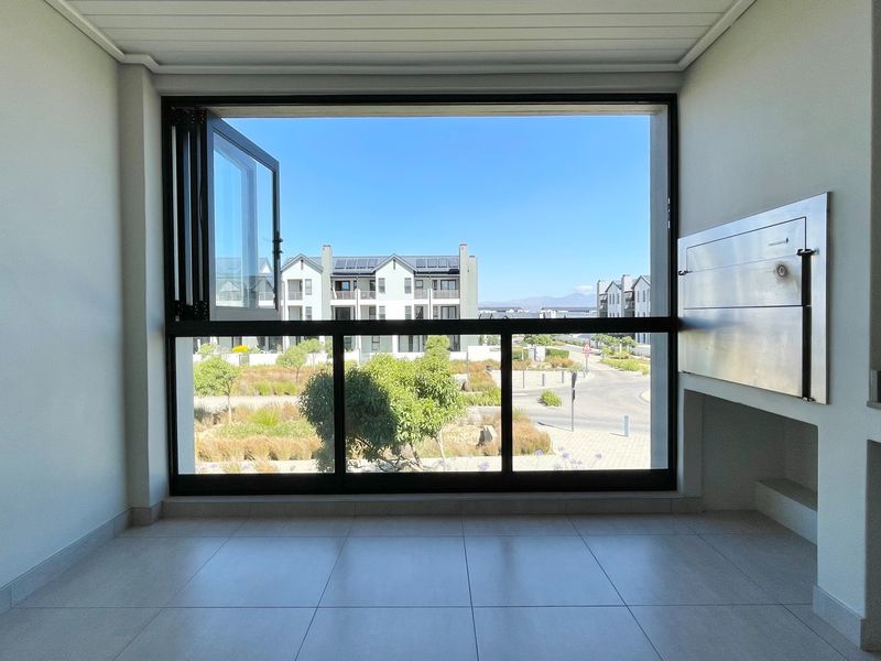 A bright, empty balcony featuring tiled flooring, a built-in braai, and large glass doors offering a clear view of the surrounding estate.