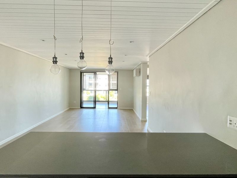 Spacious open-plan living area featuring modern pendant lighting, neutral finishes, and large sliding glass doors leading to an outdoor space.
