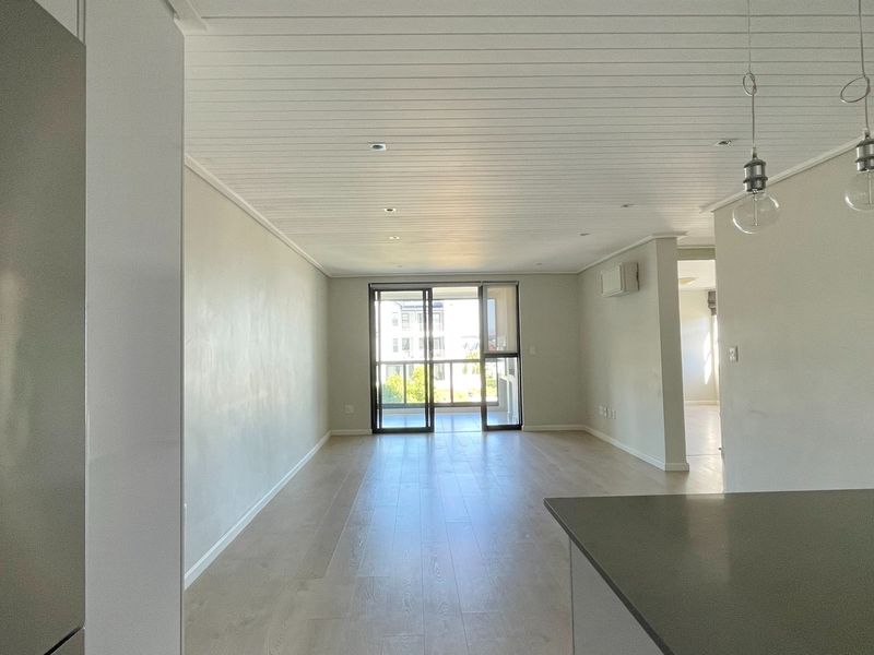 Spacious open-plan living area featuring modern laminate flooring, a unique tongue and groove ceiling, and direct access to a private balcony.