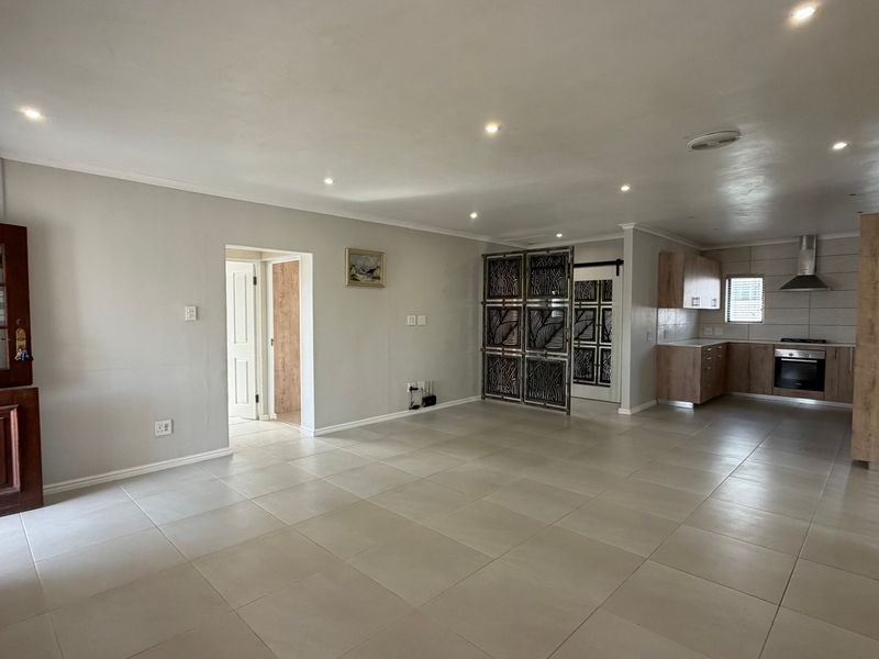Spacious open-plan living area featuring tiled floors, recessed lighting, and a modern kitchen with built-in cabinetry, oven, and extractor fan.