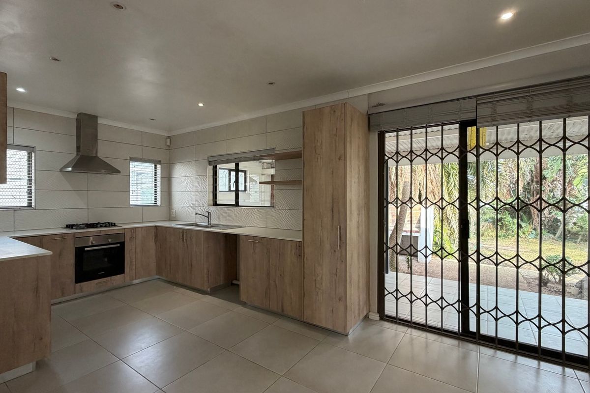 Modern kitchen featuring light wood cabinetry, built-in oven, gas hob, and direct access to the outdoor patio through a secure sliding door.
