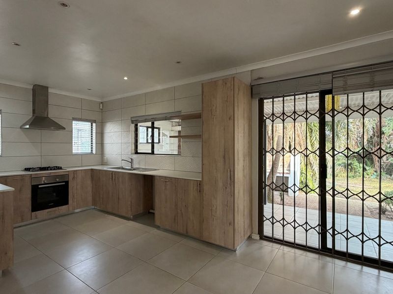 Modern kitchen featuring light wood cabinetry, built-in oven, gas hob, and direct access to the outdoor patio through a secure sliding door.