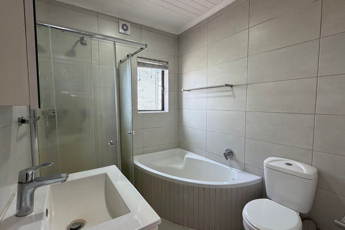 A clean, functional bathroom featuring a built-in bathtub, separate shower enclosure, vanity basin, and toilet with neutral wall tiling.