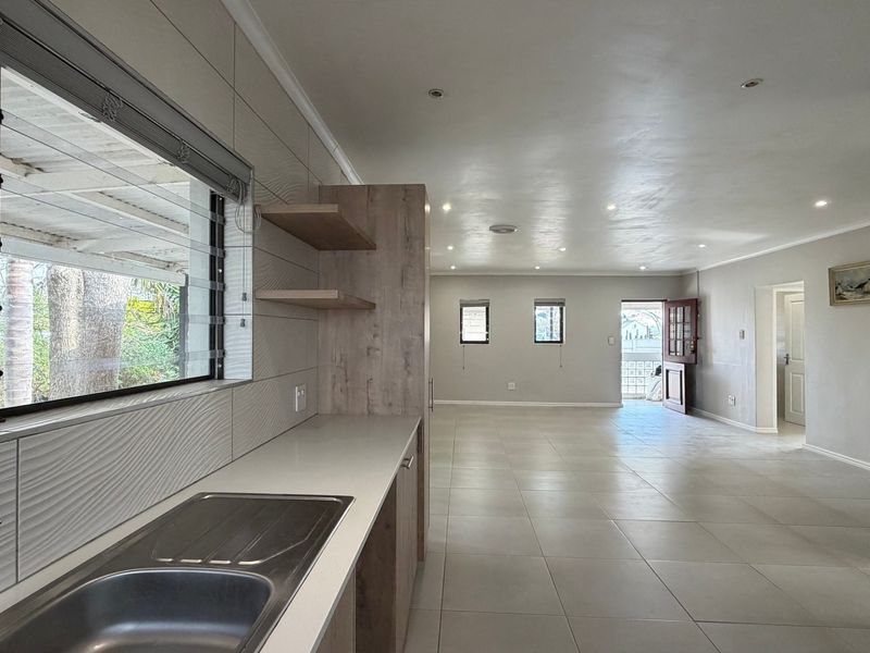 Spacious open-plan living area featuring modern tiled flooring, recessed lighting, and a functional kitchen workspace with a stainless steel sink and built-in cabinetry.