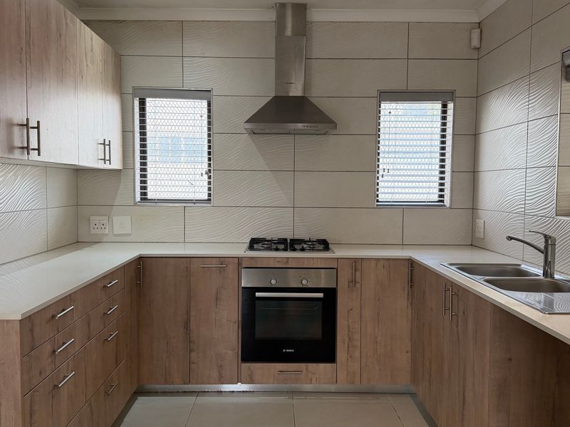 A modern, well-maintained kitchen featuring wood-finish cabinetry, stone countertops, built-in stainless steel appliances, and a tiled splashback.
