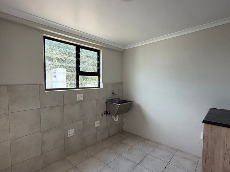 A functional laundry area featuring a stainless steel utility sink, tiled splashback, tiled flooring, and plumbing connections for laundry appliances.