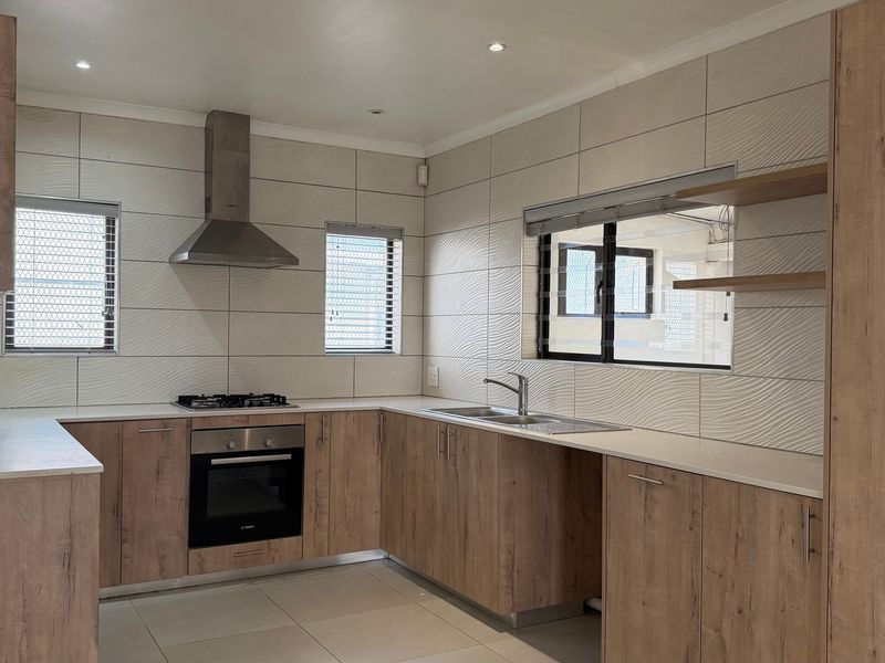 Modern kitchen featuring wood-look cabinetry, stone countertops, integrated gas hob, oven, extractor fan, and tiled splashback with recessed lighting.