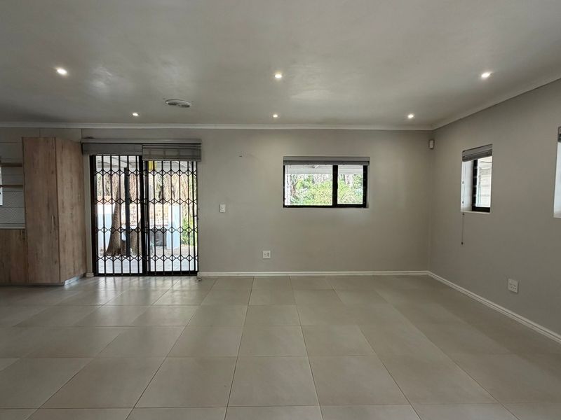 Spacious open-plan living area featuring neutral tiled flooring, recessed downlights, and direct access to the exterior through a secure sliding gate.