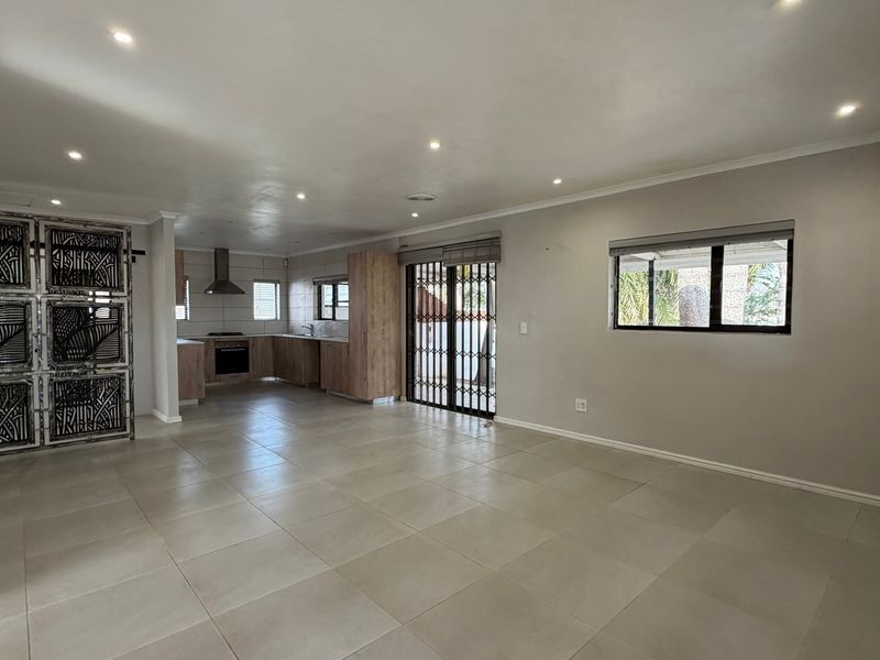 Spacious open-plan living area featuring neutral tiled flooring, recessed lighting, and a modern kitchen with built-in cabinetry and appliances.