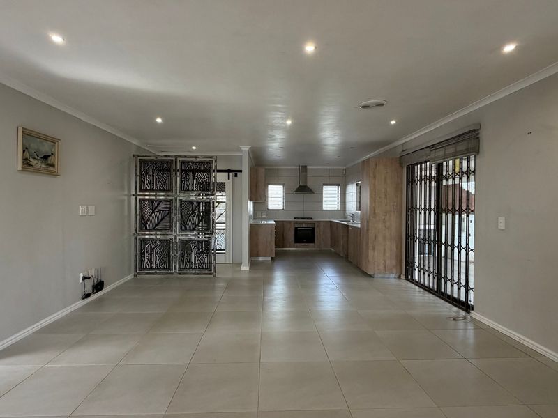 Spacious open-plan living and kitchen area featuring neutral tiled flooring, recessed lighting, and modern wood-finish cabinetry with integrated appliances.