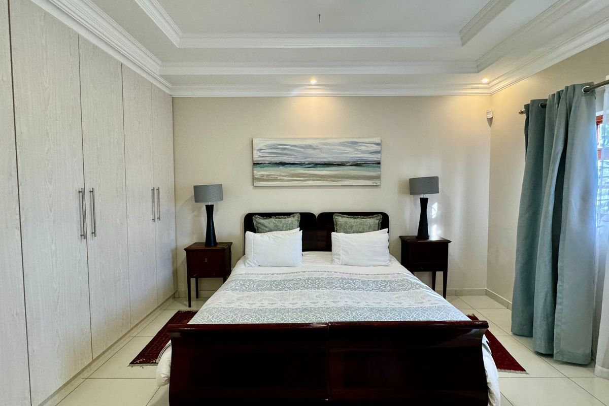 A well-maintained bedroom featuring extensive built-in cupboards, a decorative tray ceiling with recessed lighting, and neutral tiled flooring.