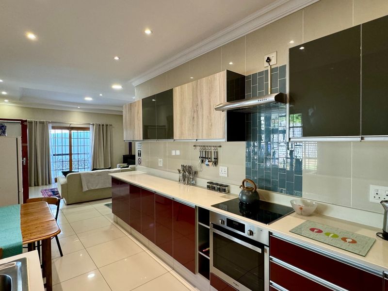 Modern open-plan kitchen featuring high-gloss cabinetry, stone countertops, integrated appliances, and tiled flooring, seamlessly flowing into the adjacent living area.