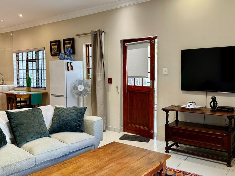 An open-plan living and kitchen area featuring tiled floors, recessed lighting, and a timber exterior door leading to the outside.
