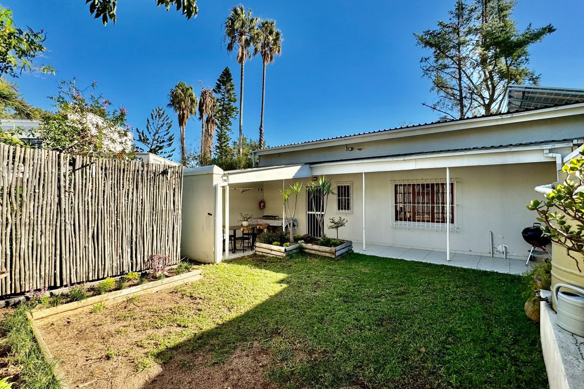 Rear view of the cottage featuring a covered patio, a small lawn area with raised garden beds, and a timber privacy screen.