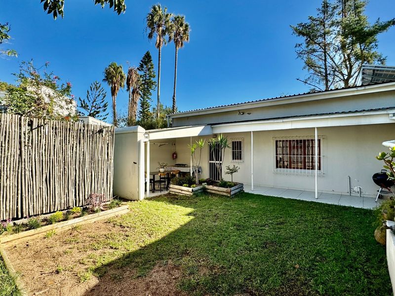 Rear view of the cottage featuring a covered patio, a small lawn area with raised garden beds, and a timber privacy screen.