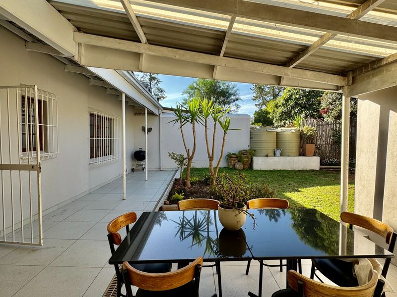 A covered outdoor patio area featuring tiled flooring, security fixtures, and direct access to a private garden with water storage tanks.
