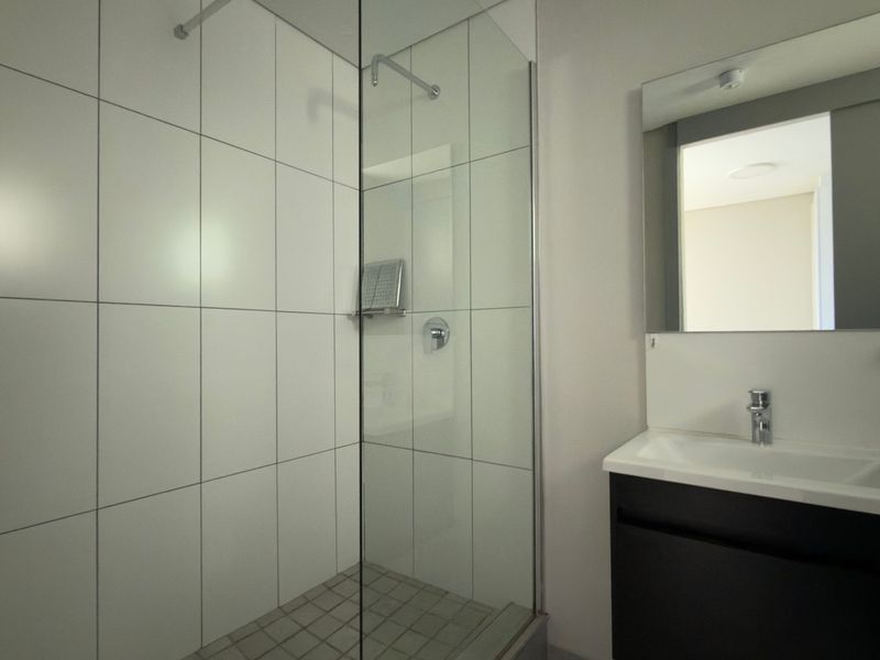 Modern bathroom featuring a glass-enclosed shower with white wall tiles and a sleek vanity unit with an integrated basin and mirror.
