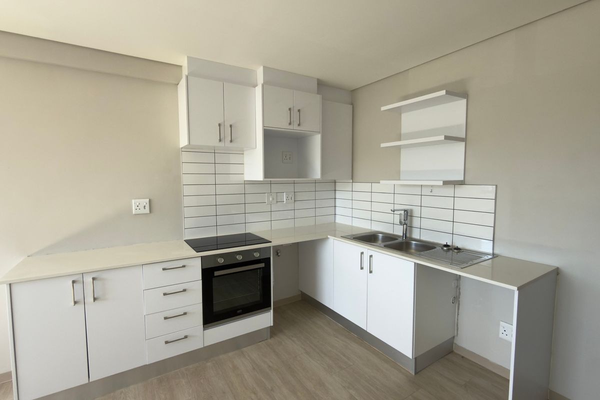 A clean, modern kitchen featuring white cabinetry, subway tile backsplash, built-in oven and hob, and double sink with laminate flooring.