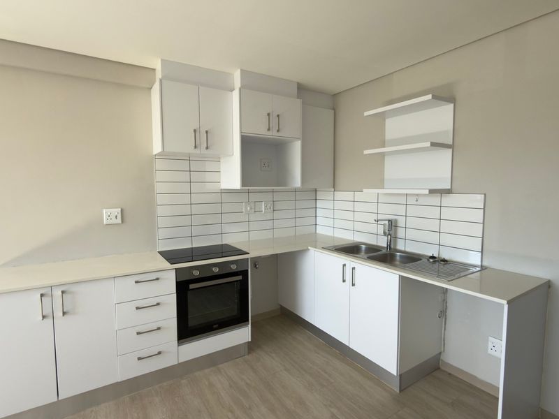 A clean, modern kitchen featuring white cabinetry, subway tile backsplash, built-in oven and hob, and double sink with laminate flooring.