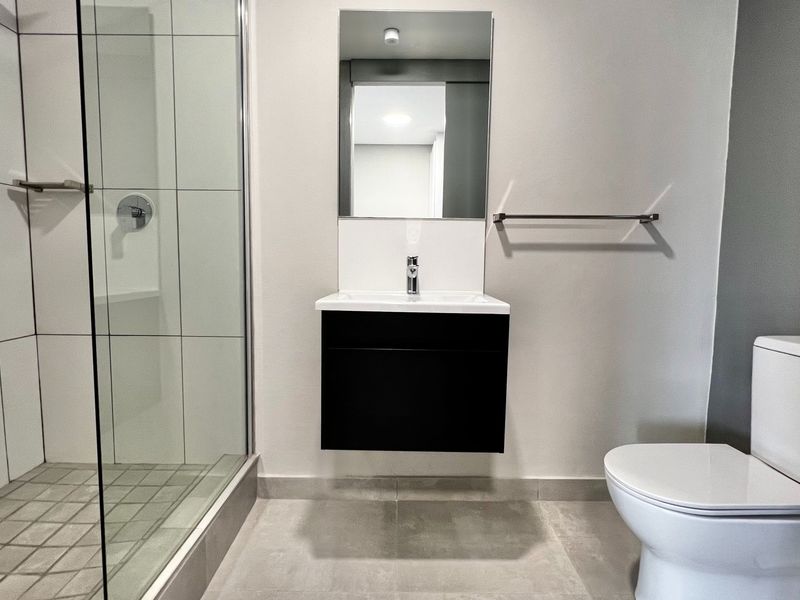 Modern bathroom featuring a walk-in shower with glass enclosure, wall-mounted vanity with basin, and a clean, contemporary tiled finish.