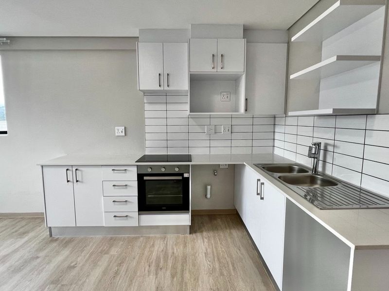 Modern kitchen featuring white cabinetry, subway tile backsplash, integrated electric oven and hob, and a stainless steel double sink with laminate flooring.