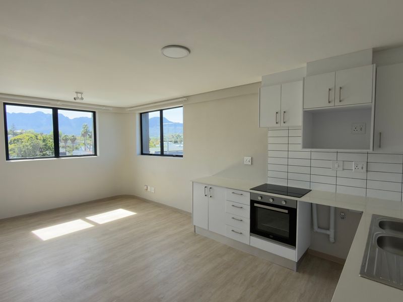 Bright open-plan living area featuring a modern kitchen with built-in oven, hob, and double sink, complemented by laminate flooring and mountain views.