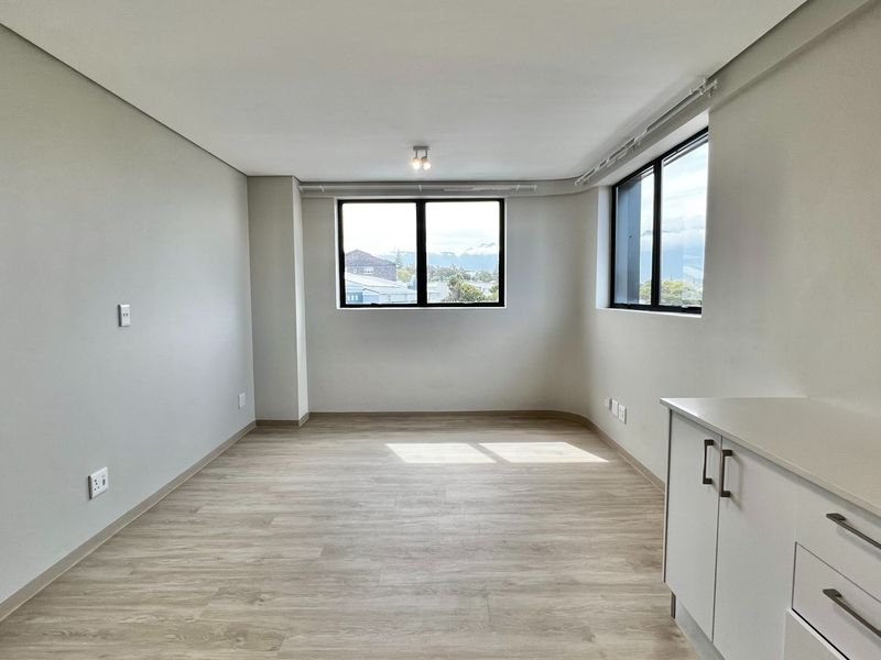 A bright, modern open-plan living area featuring light laminate flooring, neutral walls, and built-in cabinetry, offering a clean and versatile space.