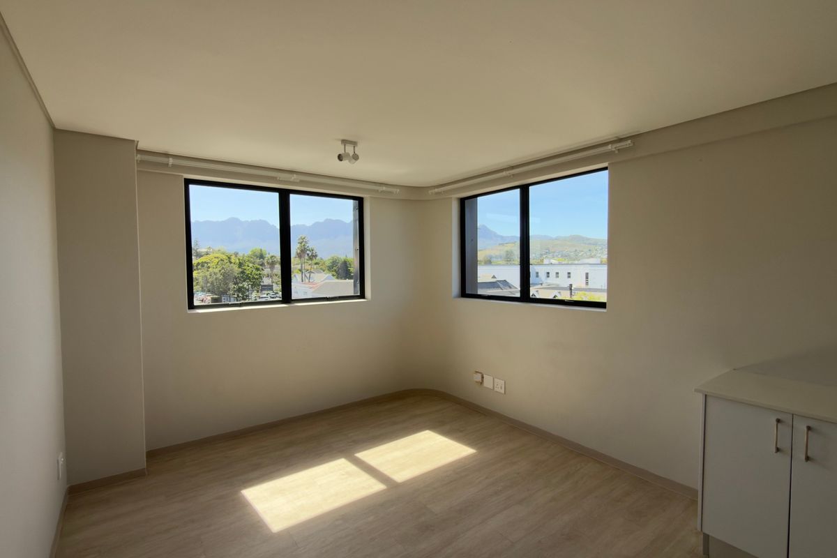 A bright, empty living area featuring modern laminate flooring, neutral walls, and large windows offering scenic mountain views.