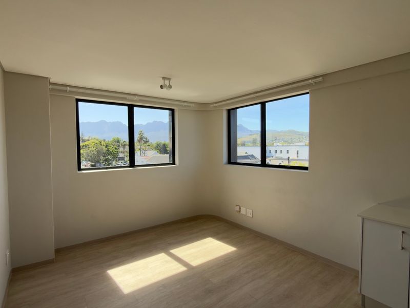 A bright, empty living area featuring modern laminate flooring, neutral walls, and large windows offering scenic mountain views.
