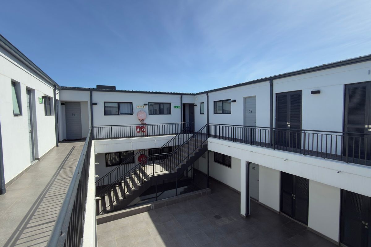 An exterior view of an apartment complex courtyard featuring a metal staircase, tiled walkways, and multiple unit entrances with secure railings.