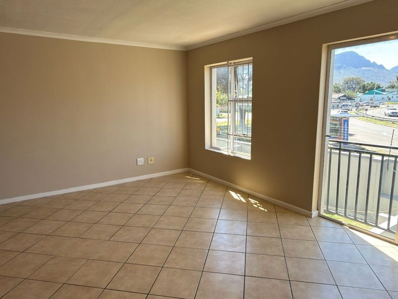 An empty open-plan living area featuring tiled floors, a sliding door to a balcony, and a built-in oven, offering a bright and functional space.