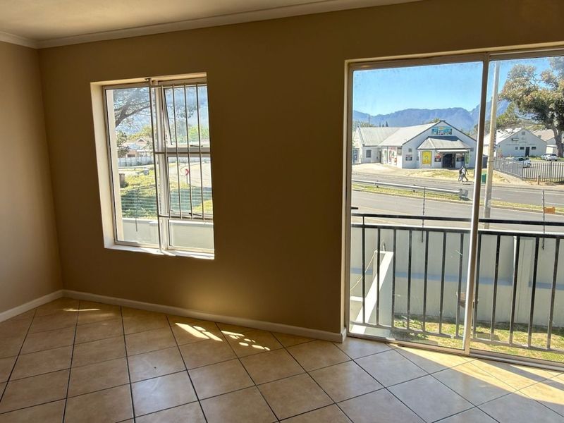 An empty living room featuring tiled flooring, large windows with security bars, and a sliding glass door leading to a balcony with street views.