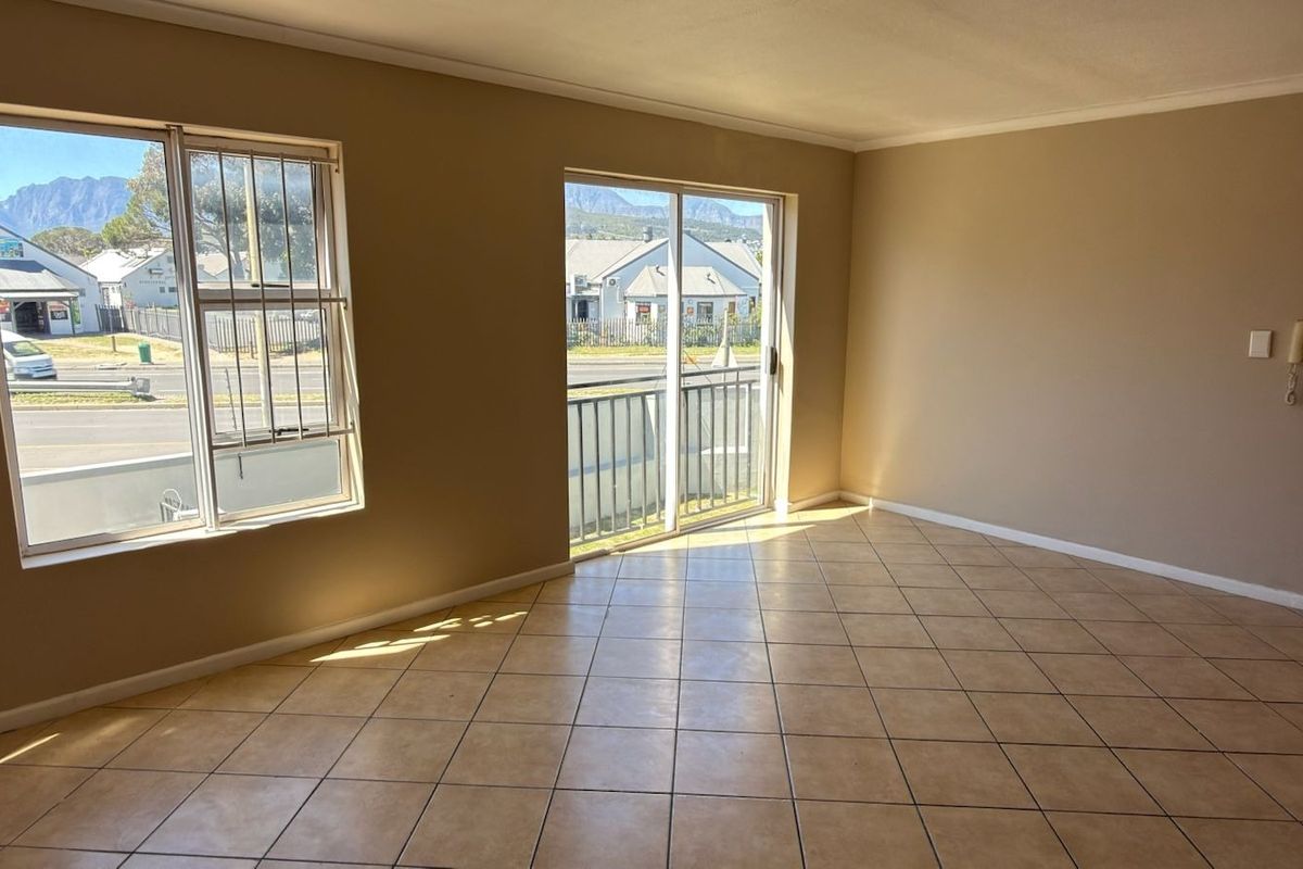 A bright, empty living room featuring neutral tiled flooring, large windows with security bars, and a sliding glass door leading to a balcony.