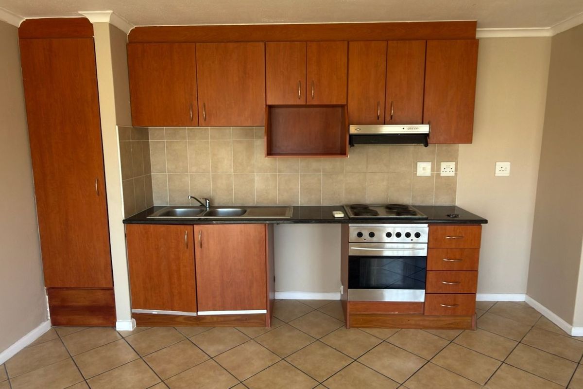 A functional kitchen featuring wood-finish cabinetry, tiled backsplash, built-in oven and hob, and tiled flooring in a clean, open-plan layout.
