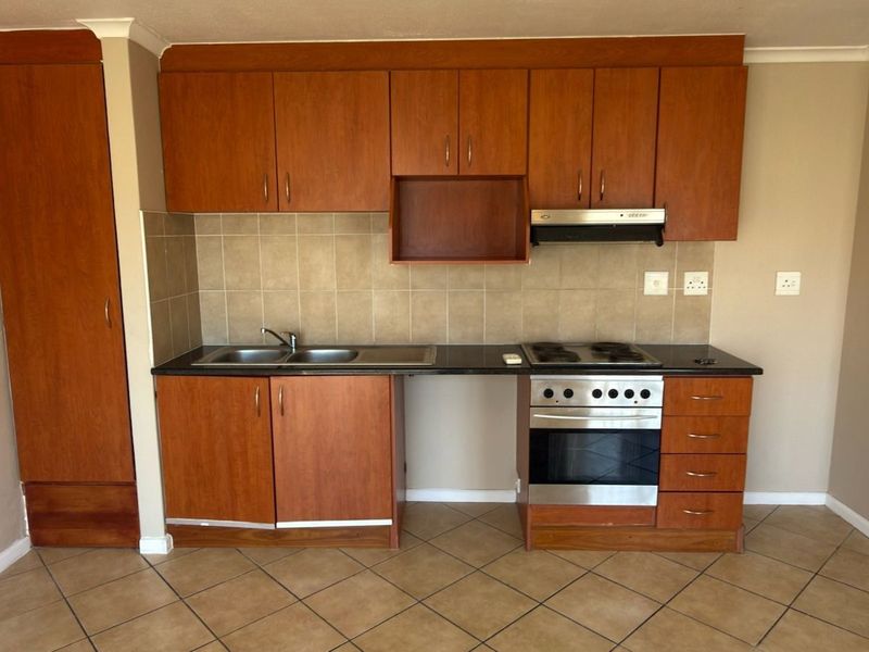 A functional kitchen featuring wood-finish cabinetry, tiled backsplash, built-in oven and hob, and tiled flooring in a clean, open-plan layout.