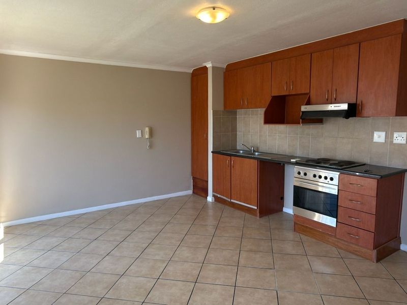 An open-plan kitchen and living area featuring wooden cabinetry, built-in appliances, tiled flooring, and access to a balcony through sliding glass doors.