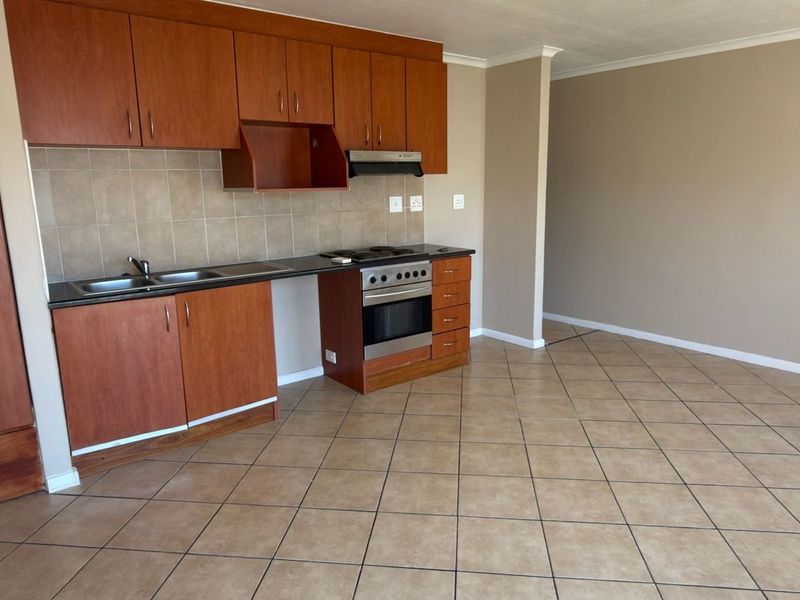 An open-plan kitchen area featuring wooden cabinetry, laminate countertops, a built-in oven, and tiled flooring in a neutral, well-maintained space.