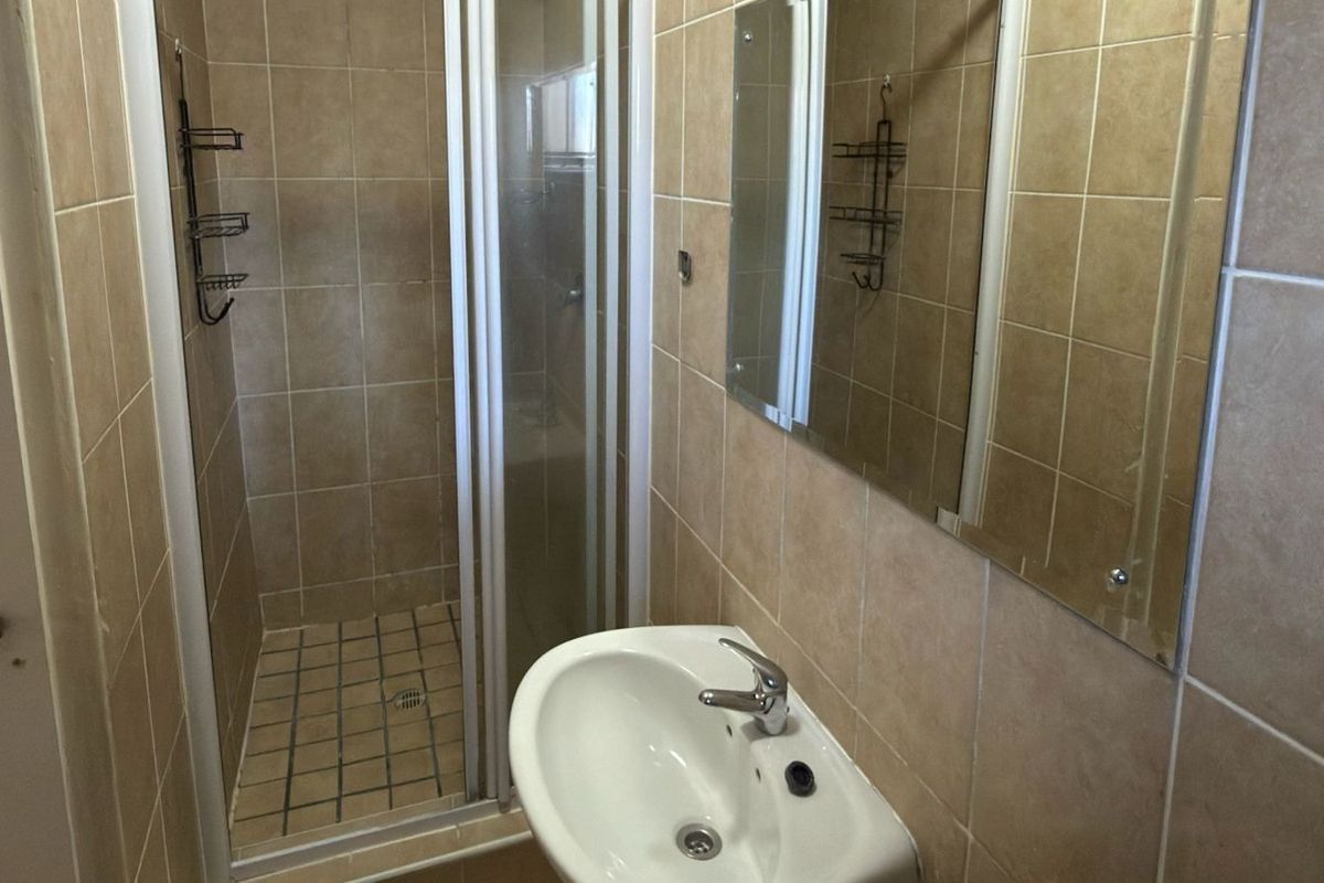 A functional bathroom featuring a shower enclosure, wall-mounted basin with mixer tap, and tiled wall finishes.