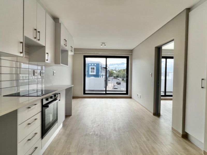 Modern open-plan kitchen and living area featuring sleek white cabinetry, integrated appliances, subway tile backsplash, and light wood-look flooring with access to a balcony.