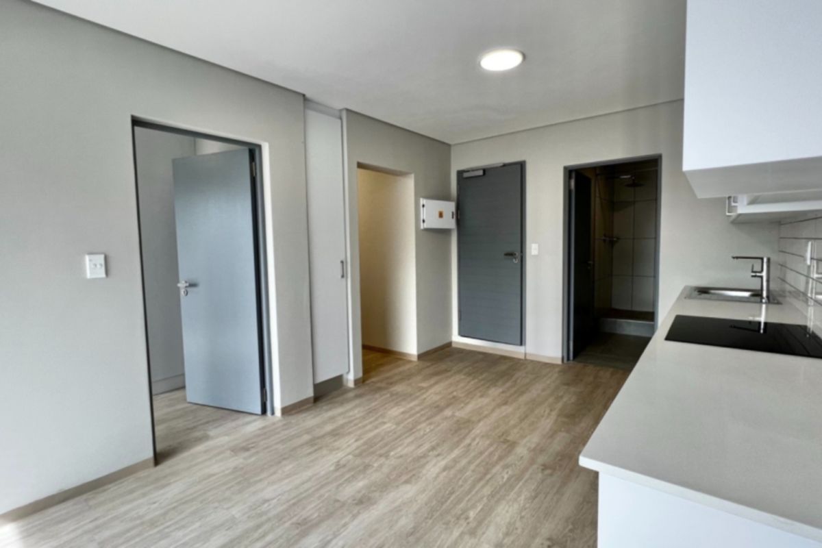 Modern open-plan apartment living area featuring a sleek kitchen with stone countertops, electric hob, and neutral finishes throughout.