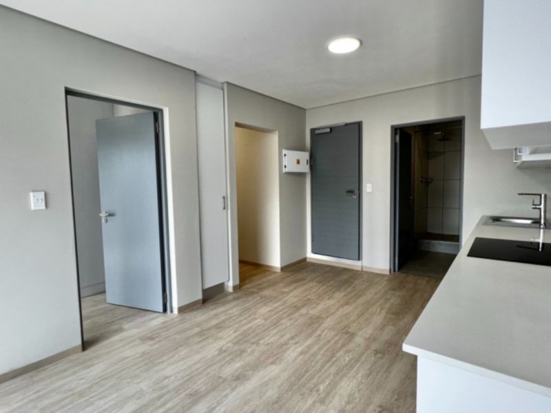 Modern open-plan apartment living area featuring a sleek kitchen with stone countertops, electric hob, and neutral finishes throughout.