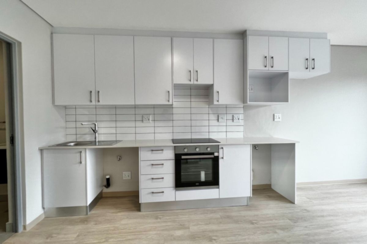 Modern, clean-lined kitchen featuring white cabinetry, subway tile backsplash, integrated electric hob and oven, and light-toned laminate flooring in an open-plan layout.